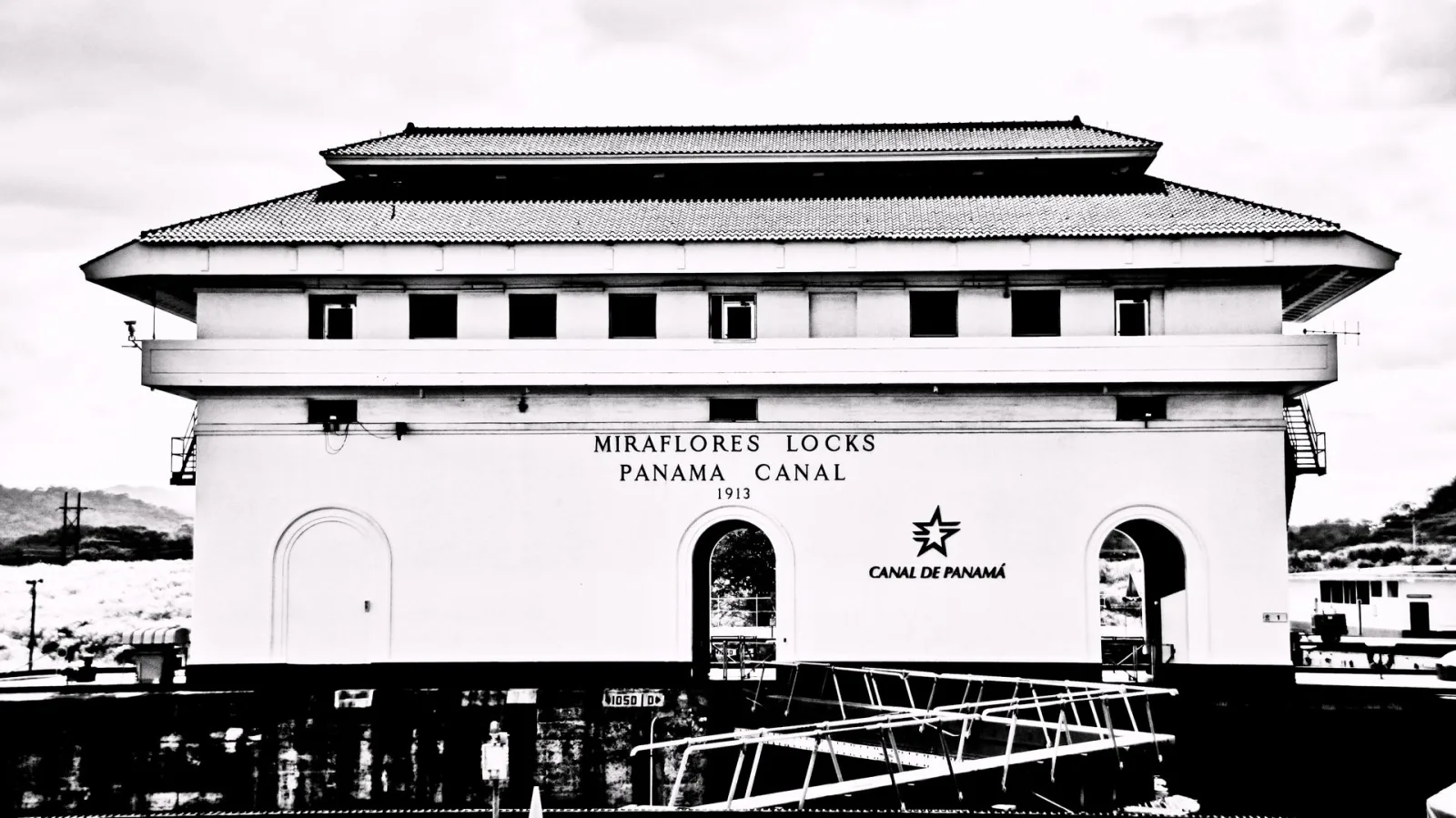 Schwarzweißes Foto des Schleusengebäudes der Miraflores-Schleusen mit weißer Fassade, Schriftzug Panama Canal und Jahreszahl 1913.