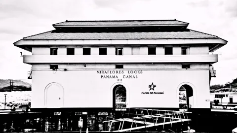 Schwarzweißes Foto des Schleusengebäudes der Miraflores-Schleusen mit weißer Fassade, Schriftzug Panama Canal und Jahreszahl 1913.