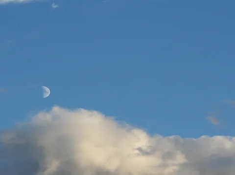Halbmond am blauen Himmel über einer großen, hell beleuchteten Wolkenbank