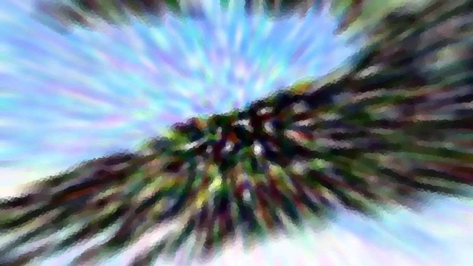 Radialer Zoom-Unschärfeeffekt: dunkles Grün von Baumkronen strahlt von der Mitte aus, am oberen Rand ist blauer Himmel mit hellen Schlieren zu sehen.