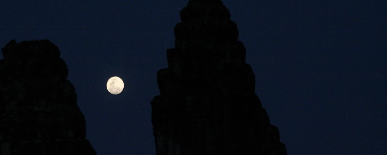 Heller Mond zwischen den dunklen Turmsilhouetten des Angkor Wat vor nachtblauem Himmel