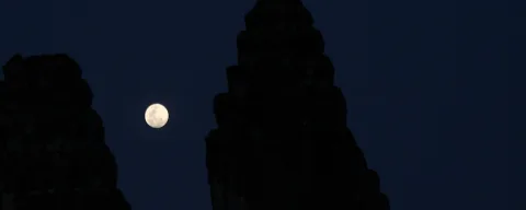 Heller Mond zwischen den dunklen Turmsilhouetten des Angkor Wat vor nachtblauem Himmel