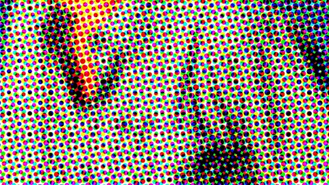 Dichtes Raster aus bunten Punkten in Rot, Gelb, Blau, Grün und Schwarz auf weißem Grund, dunkle Punktgruppen ziehen diagonal durchs Bild.