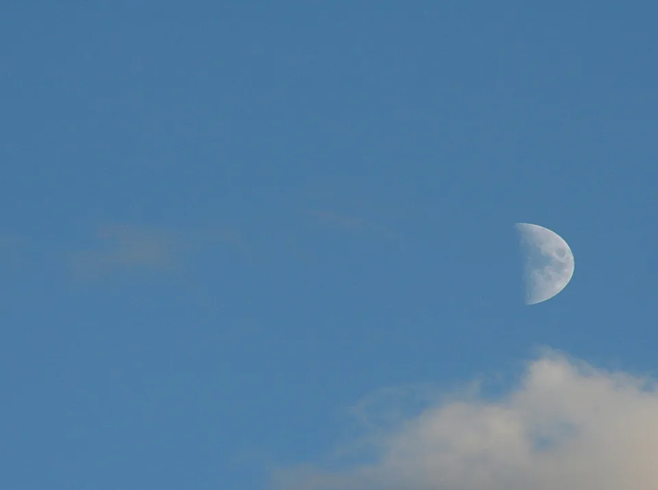 Ein halber Mond leuchtet am tiefblauen Himmel rechts neben der Bildmitte, unten rechts zieht eine helle Wolkenbank ins Bild.
