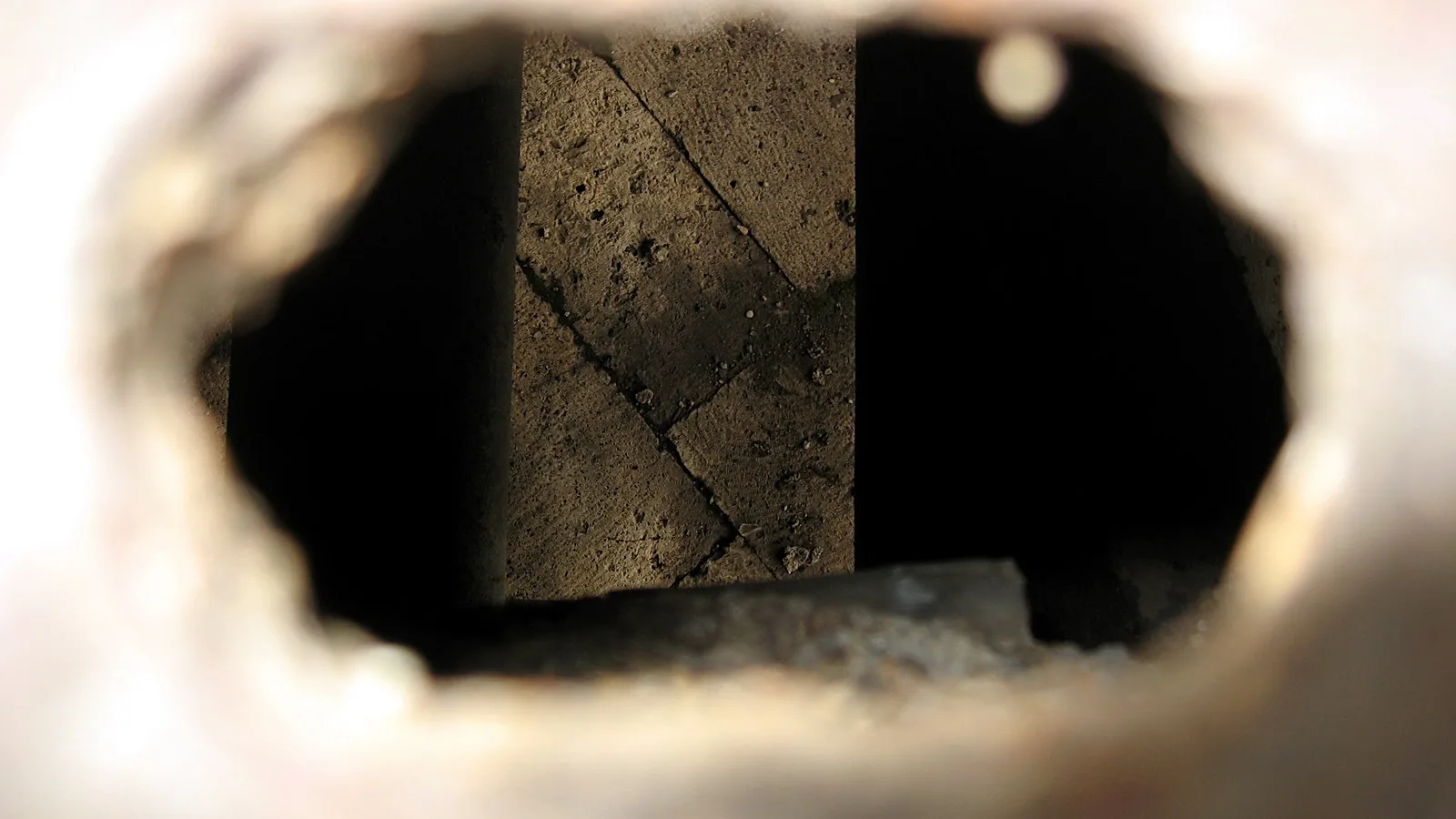 Blick durch eine runde Öffnung auf eine rissige Steinmauer mit dunklem Innenraum.