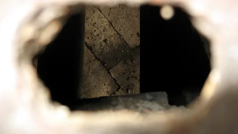Blick durch eine runde Öffnung auf eine rissige Steinmauer mit dunklem Innenraum.