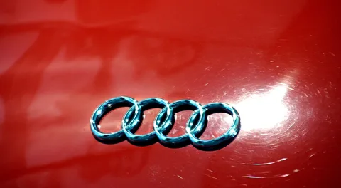 Chromfarbenes Audi-Logo mit vier ineinander verschlungenen Ringen auf einer roten, glänzenden Karosserie.