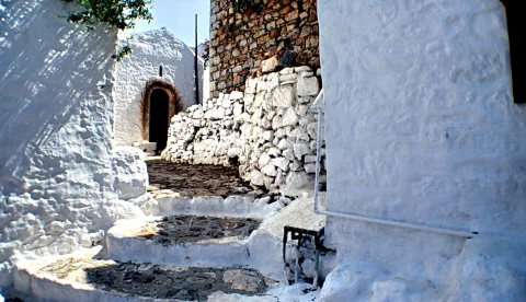 Enge Gasse mit weiß getünchten Mauern, einer Steintreppe und einer kleinen Kapelle mit Rundbogentür im Schatten.