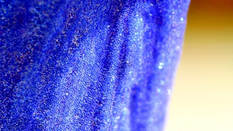 Makroaufnahme eines blauen Blütenblatts mit feiner körniger Oberflächenstruktur und Falten, rechts ein gelblich verschwommener Hintergrund.