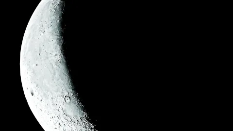 Eine Mondsichel mit zahlreichen Kratern leuchtet links im Bild, der rechte Teil liegt im schwarzen Weltraum.