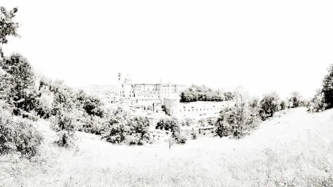 Panoramablick auf die Hügelstadt Urbino mit großem Palast und Türmen, davor Bäume und eine Wiese, alles in hellen Sepiatönen.