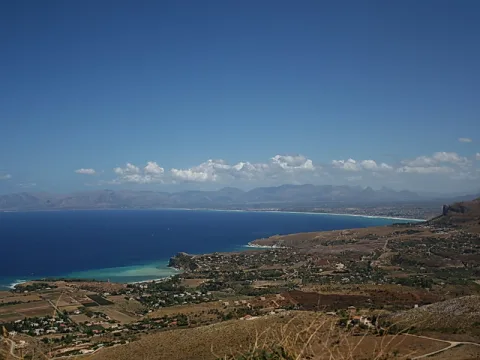 Blick über eine Bucht mit türkisfarbenem Wasser, Küstenorten und Bergen unter blauem Himmel