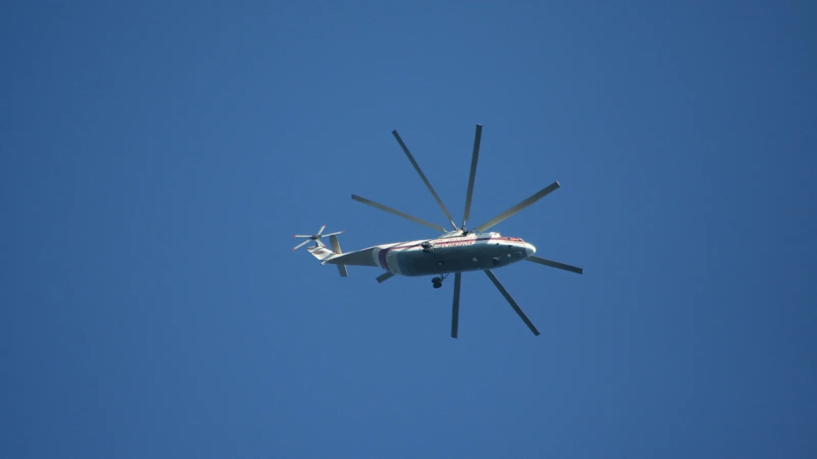 Ein weiß-roter Hubschrauber mit großem Rotor fliegt vor einem wolkenlosen blauen Himmel.