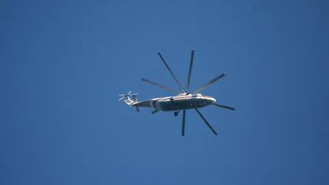 Ein weiß-roter Hubschrauber mit großem Rotor fliegt vor einem wolkenlosen blauen Himmel.