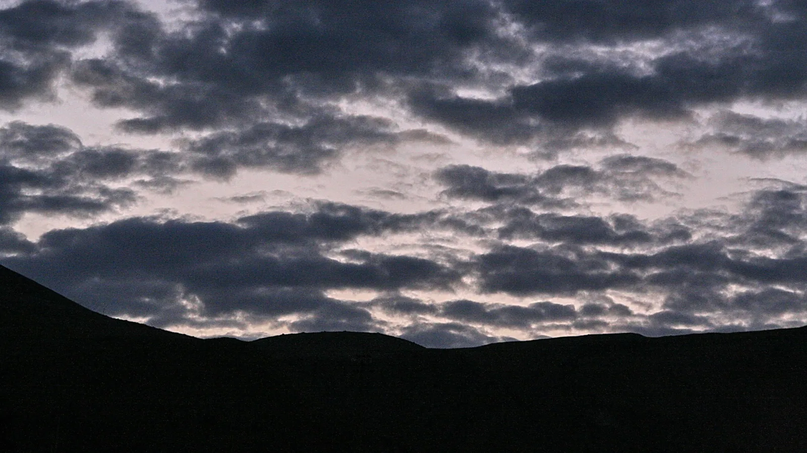 Dunkle Hügelkette vor einem Himmel mit dichten, grauen Wolken am Abend.