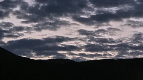 Dunkle Hügelkette vor einem Himmel mit dichten, grauen Wolken am Abend.