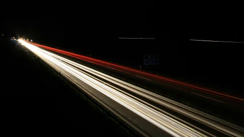Langzeitbelichtung einer nächtlichen Autobahn mit weißen Scheinwerfer- und roten Rücklichtspuren vor schwarzem Himmel.