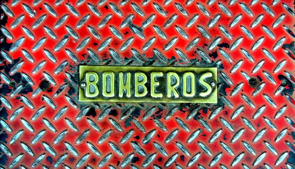 Rot lackiertes Riffelblech mit einem messingfarbenen Schild, auf dem BOMBEROS steht.