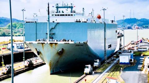 Großer grauer Frachter Curitiba fährt in eine Schleuse des Panamakanals, links und rechts ziehen Schlepploks das Schiff.