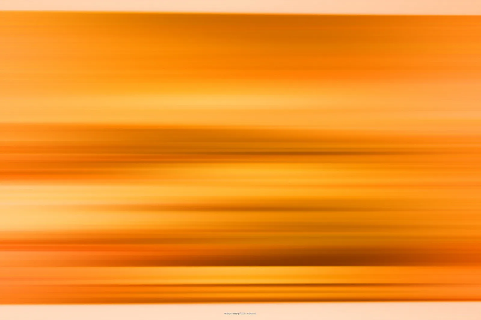 Horizontal verwischte Streifen in Orange, Gelb und Braun, die an einen Sonnenuntergang oder eine schnelle Kamerabewegung erinnern.