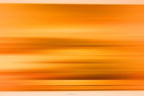 Horizontal verwischte Streifen in Orange, Gelb und Braun, die an einen Sonnenuntergang oder eine schnelle Kamerabewegung erinnern.