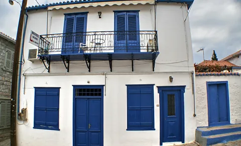 Weißes zweistöckiges Haus mit blauen Fensterläden, blauen Türen und einem Balkon mit schmiedeeisernem Geländer.