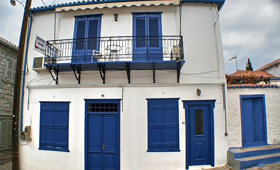Weißes zweistöckiges Haus mit blauen Fensterläden, blauen Türen und einem Balkon mit schmiedeeisernem Geländer.