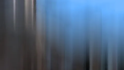 Vertikal verwischte Schlieren in Grau, Braun und Blau, oben rechts ein heller blauer Verlauf.