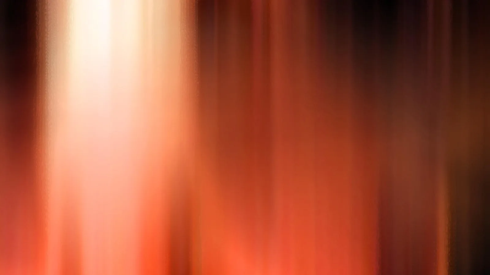 Abstrakte, stark verwischte Aufnahme mit vertikalen Streifen in Orange, Rot und Braun, links ein helles weißliches Licht, rechts dunklere Töne.