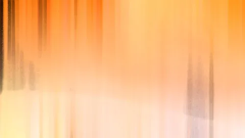 Abstrakte, vertikal verwischte Aufnahme mit warmen orangefarbenen und cremefarbenen Tönen, an den Rändern sind dunkle Schemen zu erkennen.