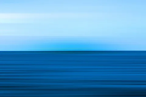 Horizontale Bewegungsunschärfe mit hellblauem Himmel und dunkelblauem Meer, der Horizont verläuft mittig durch das Bild.