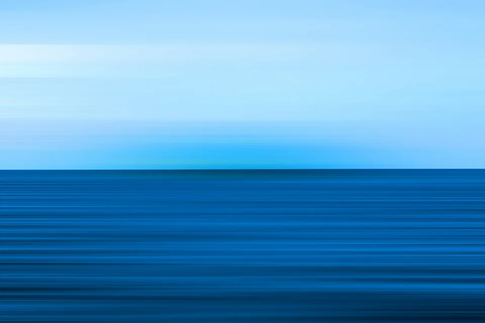 Horizontale Bewegungsunschärfe mit hellblauem Himmel und dunkelblauem Meer, der Horizont verläuft mittig durch das Bild.