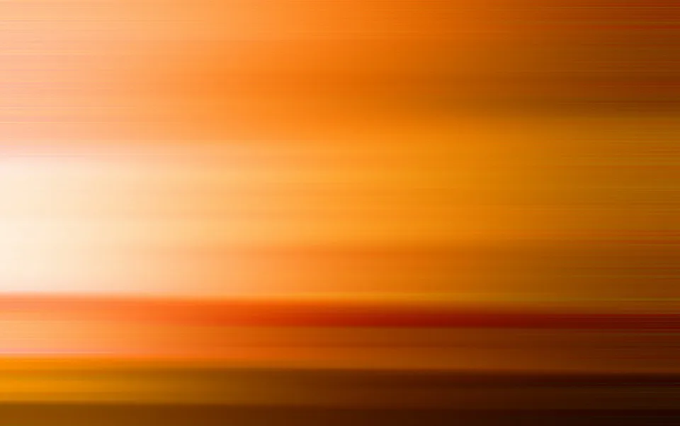 Horizontal verwischte Streifen in Orange, Gelb und Rot, links ein heller Lichtfleck, unten dunkles Braun.
