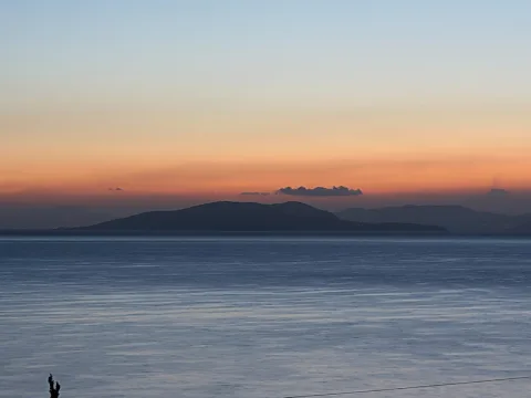 Silhouette einer Insel am Horizont über ruhigem Meer, der Himmel verläuft von Orange am Horizont in Blau.