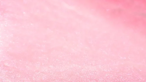 Nahaufnahme einer rosafarbenen, leicht glitzernden Oberfläche mit weichen Lichtreflexen und unscharfem Verlauf von hellem zu kräftigerem Rosa oben rechts.