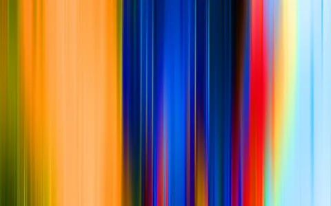 Vertikale, verwischte Streifen in Orange, Gelb, Grün, Blau, Rot und Hellblau nebeneinander, wie ein schneller Kameraschwenk über bunte Lichter.