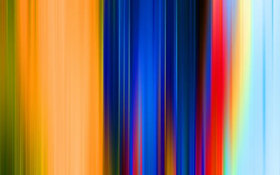 Vertikale, verwischte Streifen in Orange, Gelb, Grün, Blau, Rot und Hellblau nebeneinander, wie ein schneller Kameraschwenk über bunte Lichter.