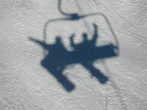 Schatten eines Sessellifts mit zwei Personen auf einer hellen Schneefläche