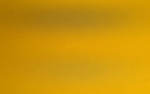Verschwommener Farbverlauf in Gelb und Ocker mit dunkleren, graubraunen Schlieren im oberen und mittleren Bereich.