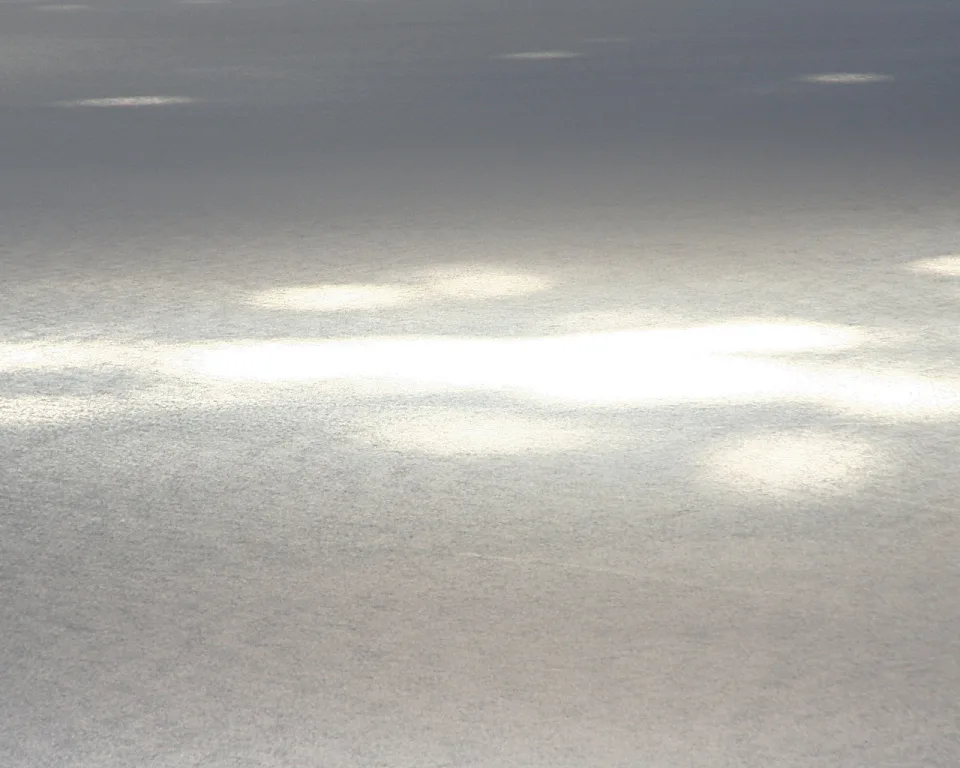 Graue, silbrig glänzende Wasseroberfläche mit hellen Sonnenreflexen