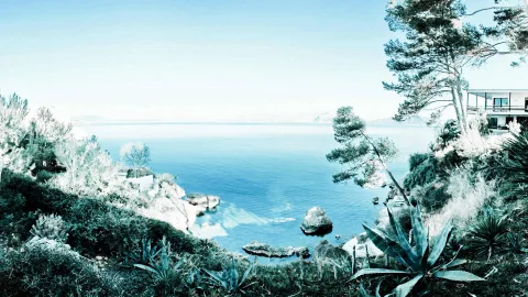 Blick auf eine blaue Meeresbucht mit Felsen, Kiefern und Agaven, rechts ein weißes Ferienhaus mit Terrasse