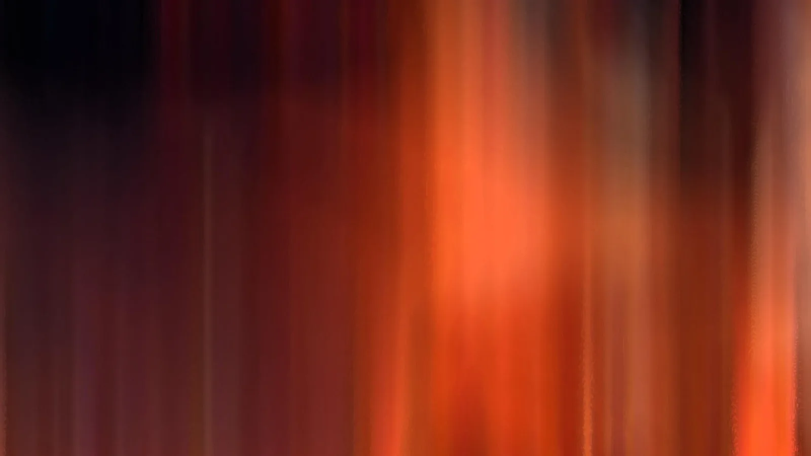Abstrakte, vertikal verwischte Schlieren in Orange, Rot und Dunkelbraun, rechts heller leuchtend, links dunkel.