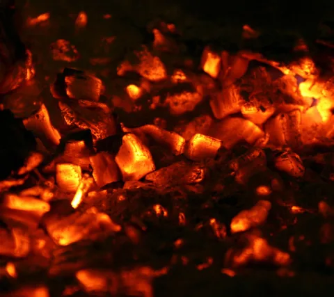 Nahaufnahme glühender Holzkohlestücke in Orange und Rot vor dunklem Hintergrund, teilweise mit heller Glut an den Kanten.