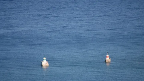 Blick aufs weite, blaue Meer mit zwei kleinen Hafenfeuern auf Betonsockeln, eines mit grün-weißem, das andere mit rot-weißem Turm.