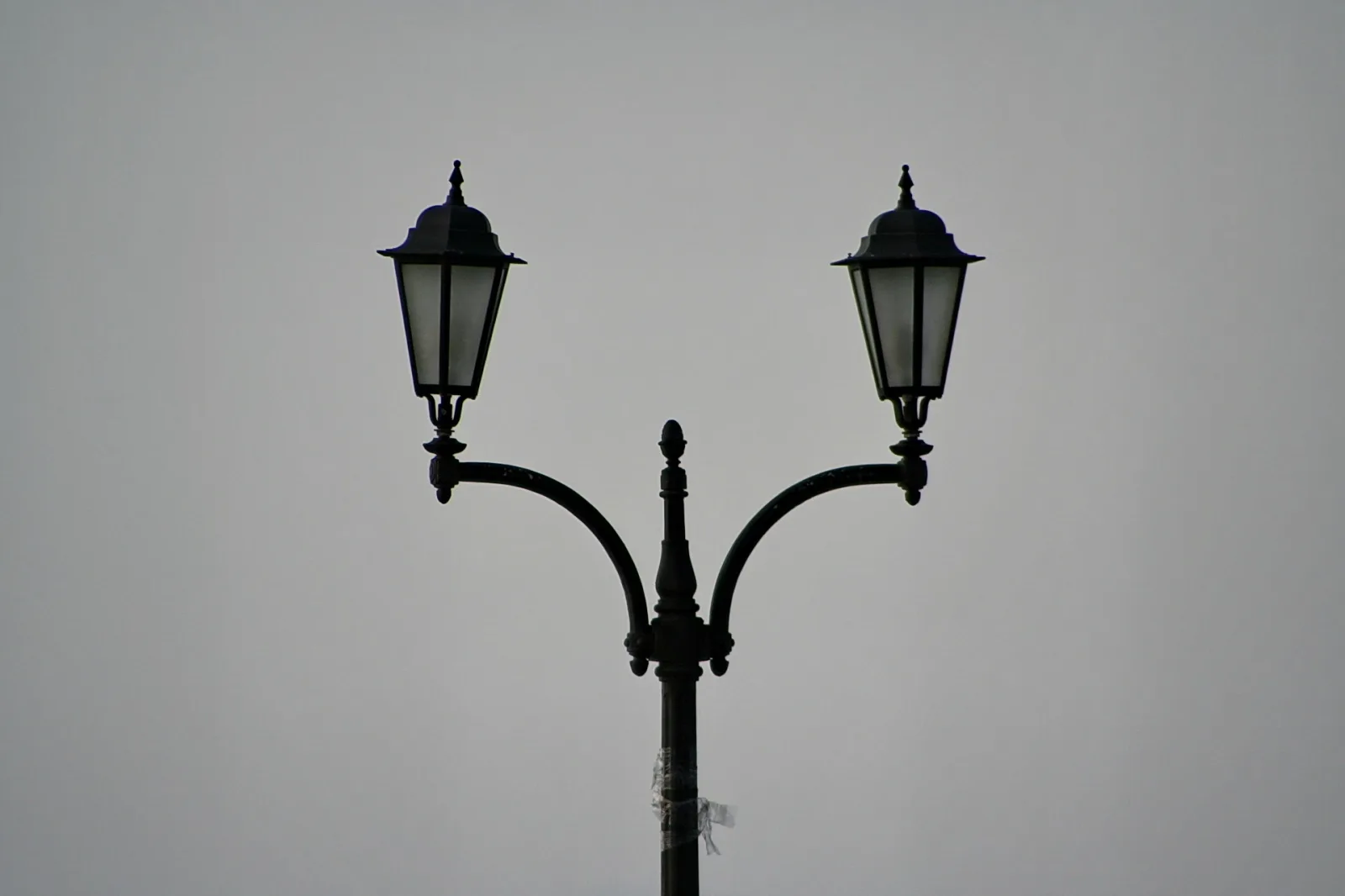 Schwarze Doppelstraßenlaterne mit zwei verglasten Laternen vor einem diesigen grauen Himmel
