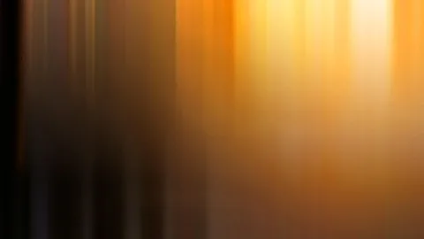 Abstrakte, vertikal verwischte Streifen in Orange und Gelb, links dunkler Hintergrund, rechts oben ein helles Leuchten.