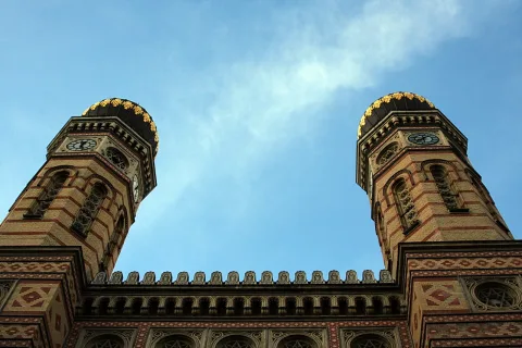 Blick von unten auf die beiden verzierten Türme einer Synagoge vor blauem Himmel.