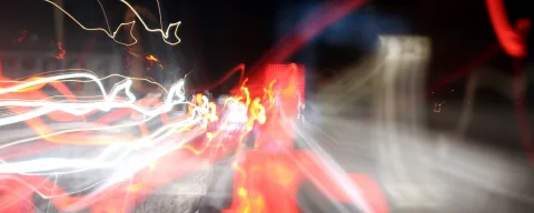 Langzeitbelichtung mit bunten Lichtspuren in Rot, Orange und Weiß vor dunklem Hintergrund, die sich wie Strahlen über das Bild ziehen.