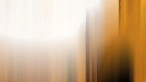 Abstrakte, vertikal verwischte Streifen in Weiß, Gold und Orange, rechts ein dunkler Schatten.