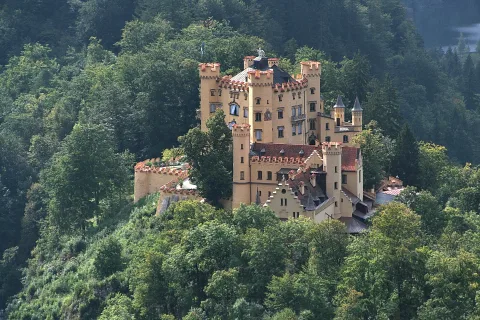 Schloss Hohenschwangau mit gelben Mauern und roten Ziegeldächern auf einem bewaldeten Hügel